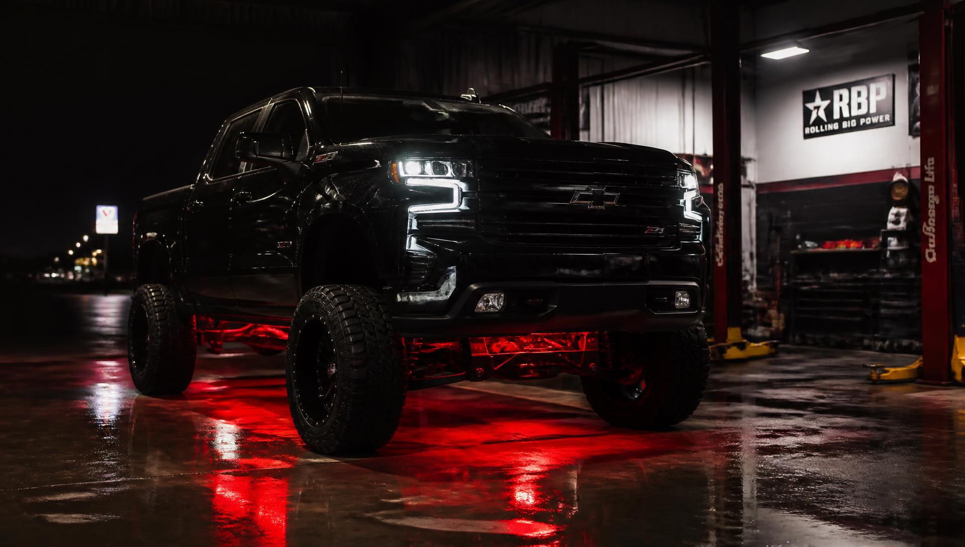 Lifted black pickup truck with red LED underglow inside the Pro Lighting Modz shop